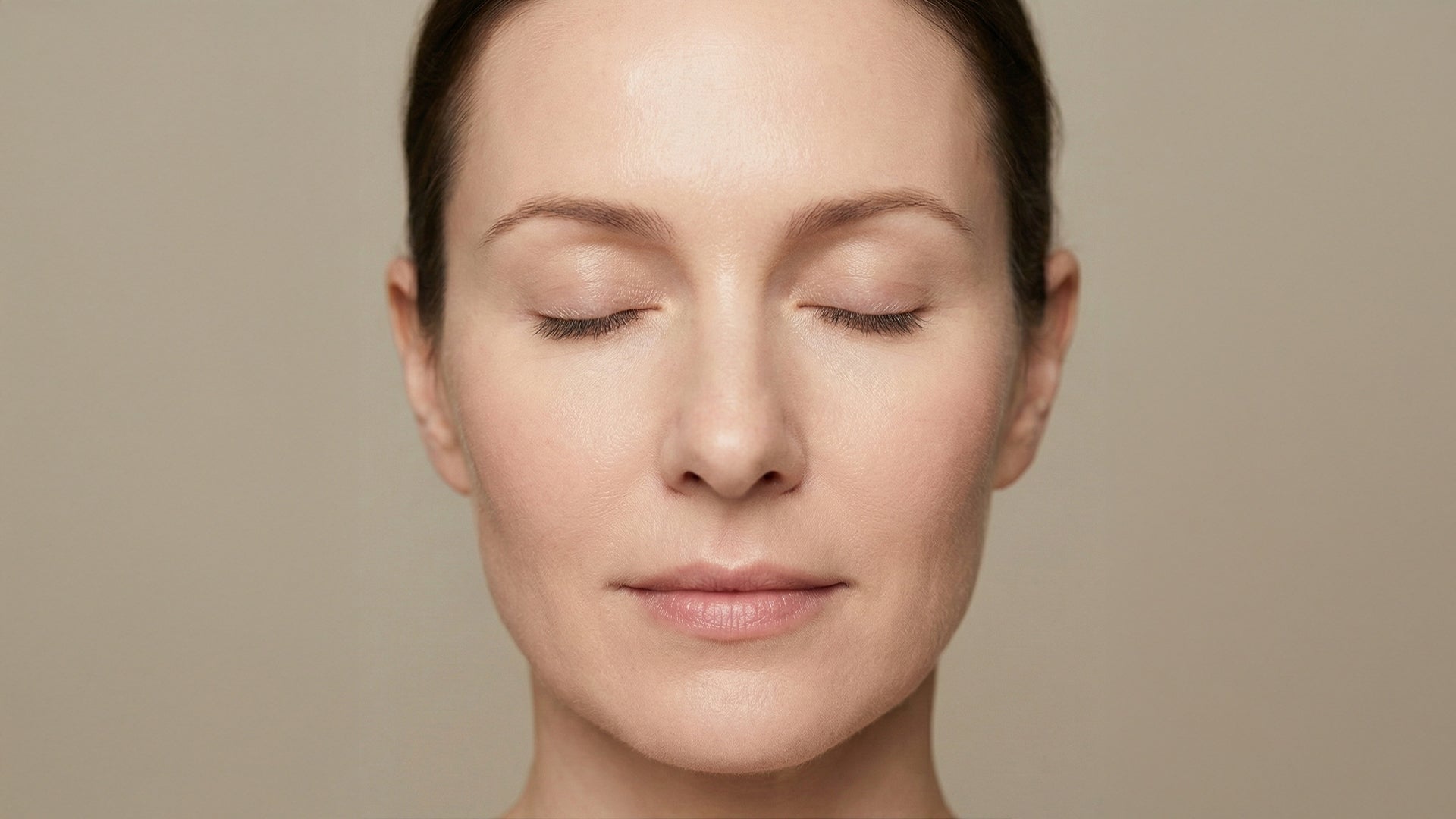 Close-up of a woman with her eyes closed against a beige background after red light therapy face treatment