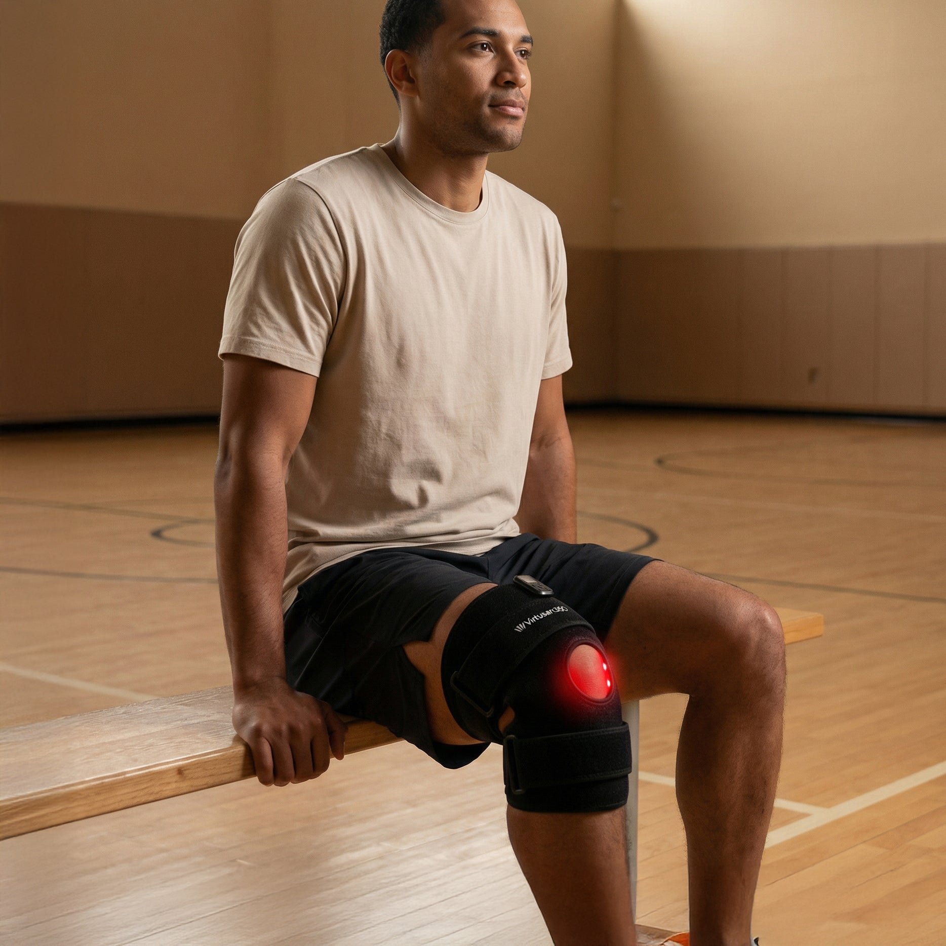 Man sitting on a basketball court with a red light therapy joint strap on his knee on his right leg