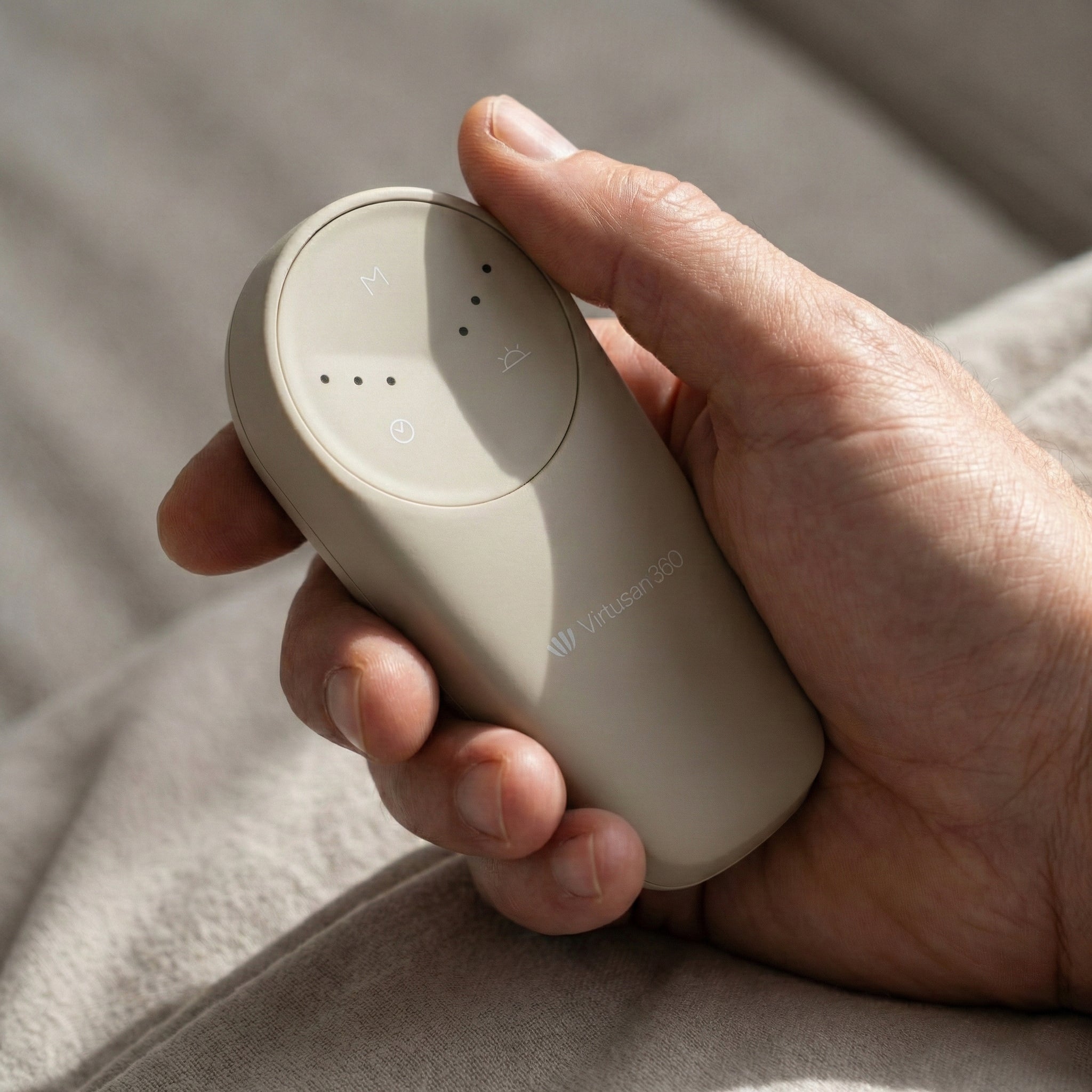 Hand holding a beige electronic remote device with 'Virtusan360' branding on a soft fabric background