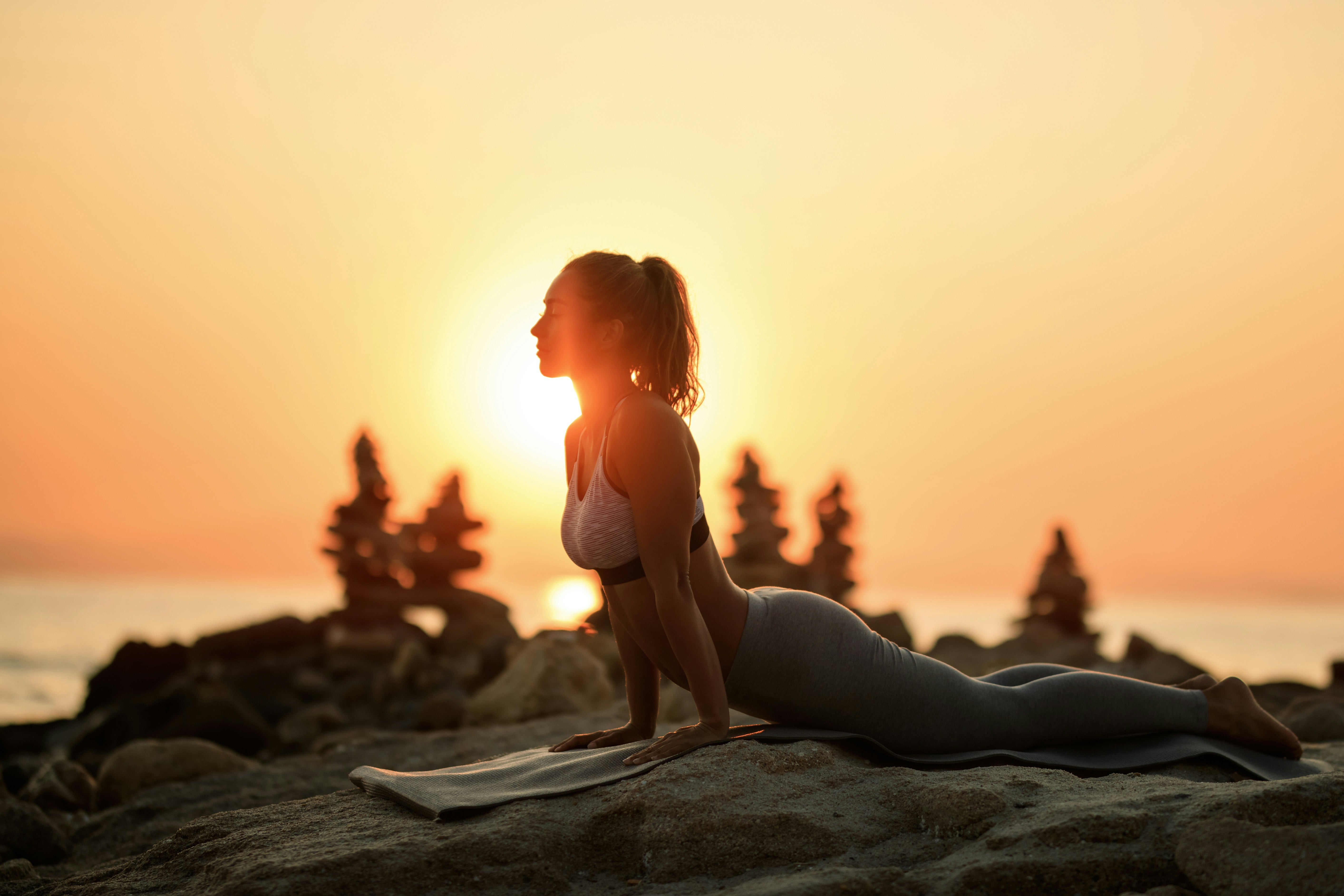 Woman practicing yoga on a rocky beach at sunset