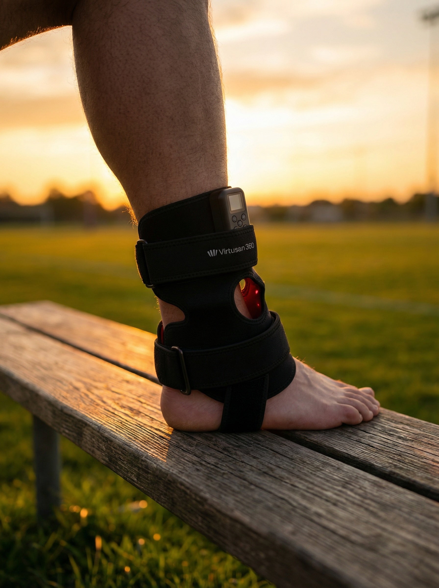 Person's foot with a black ankle support joint strap red light therapy brace on a wooden bench during sunset in Switzerland
