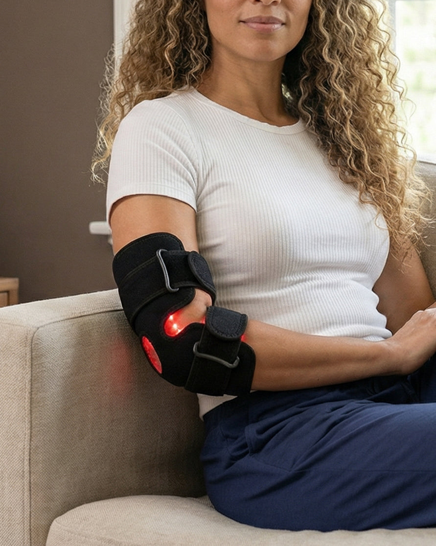 Woman sitting on a couch wearing a black Red Light Therapy Joint Strap on her arm with red lights on her wrist.
